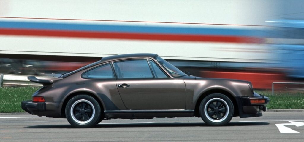 Porsche 911 Turbo (930) z boku na tle pędzącego pociągu